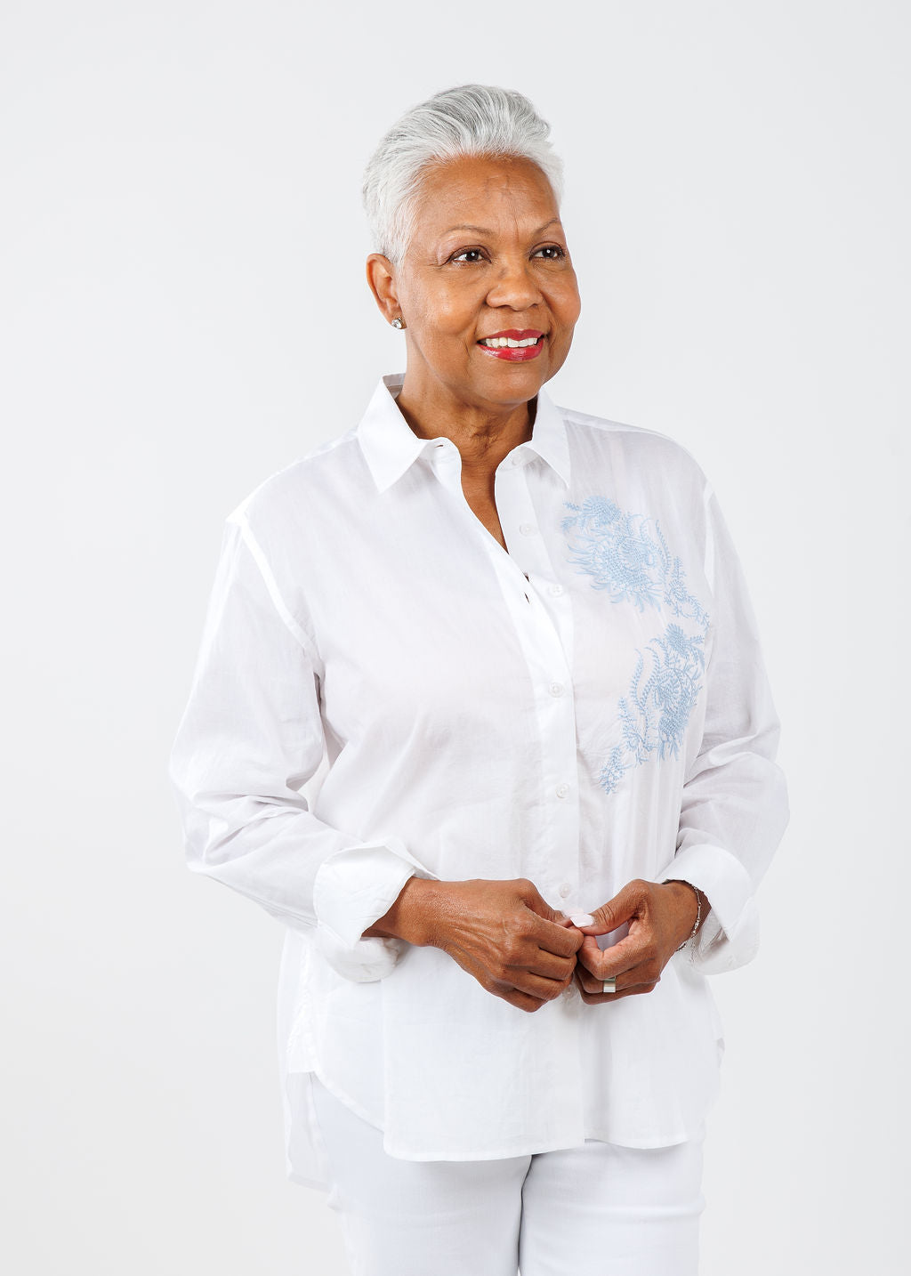 A woman modeling a white button-down shirt with light blue embroidery on the left chest area.